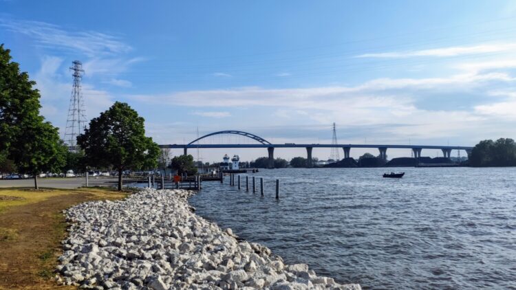a rocky river bank with a bridge over the river on a clear, sunny day