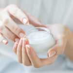 Woman dips finger in moisturizing cream