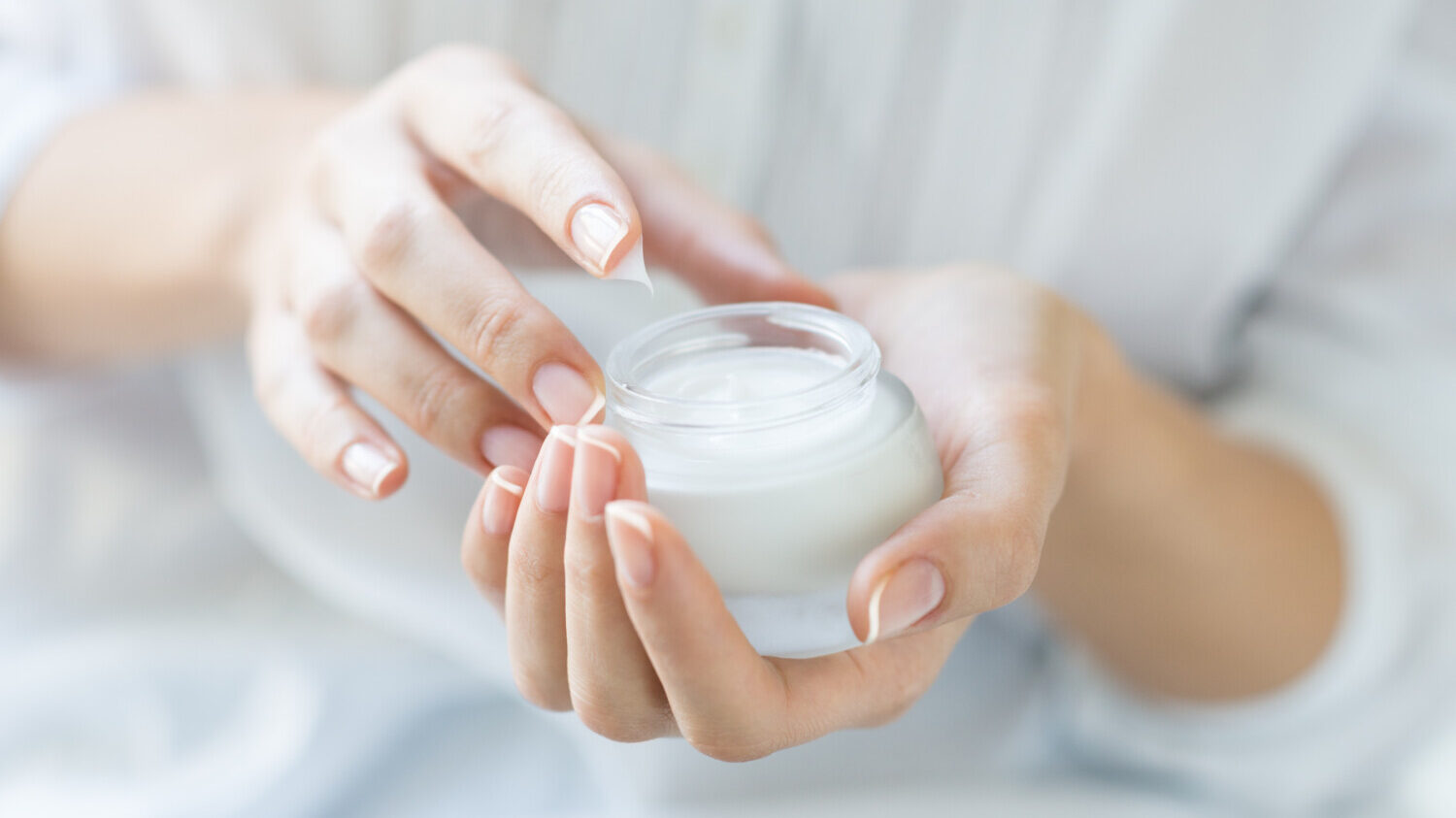 Woman dips finger in moisturizing cream