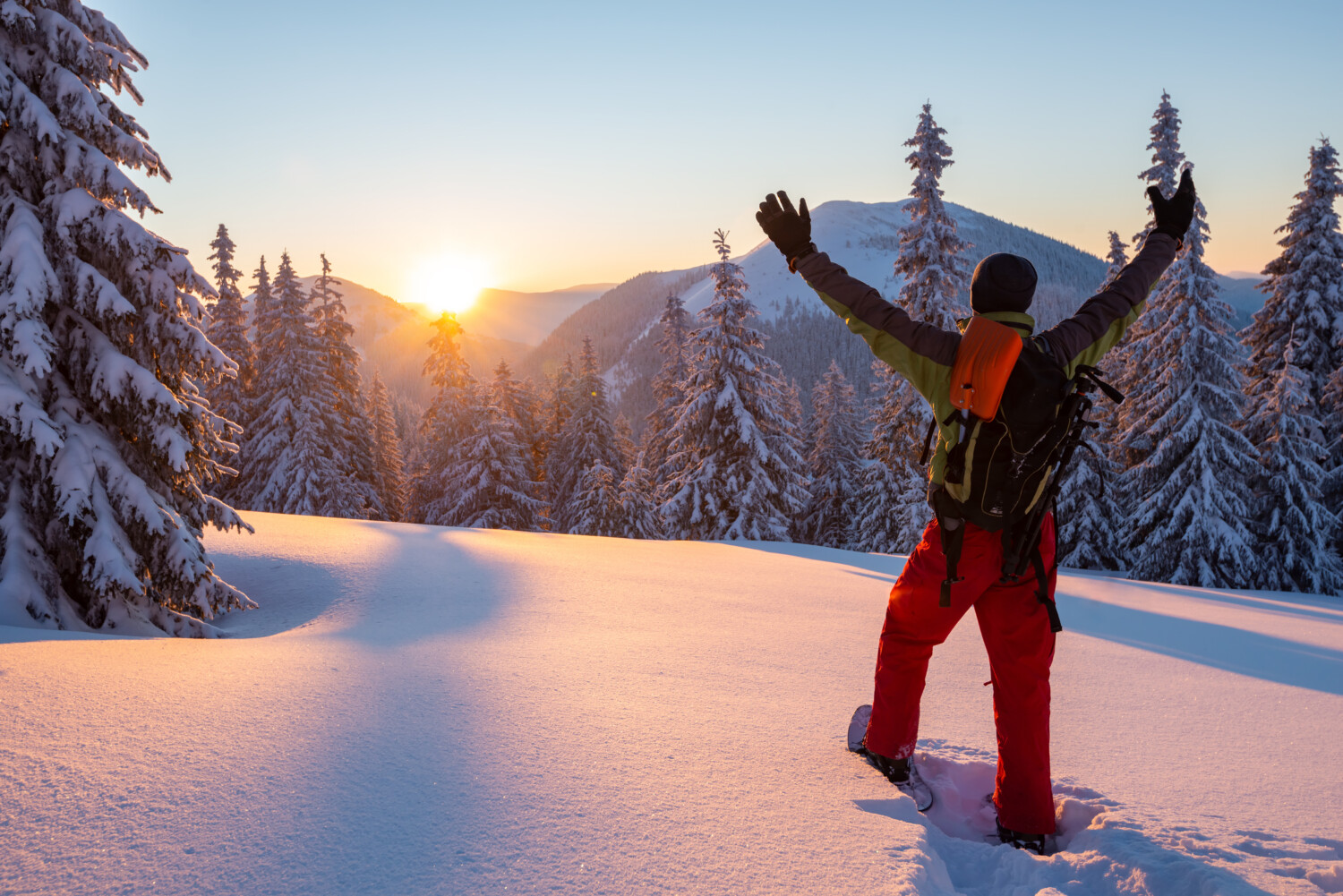 Snowshoer enjoys winter landscape with raised arms