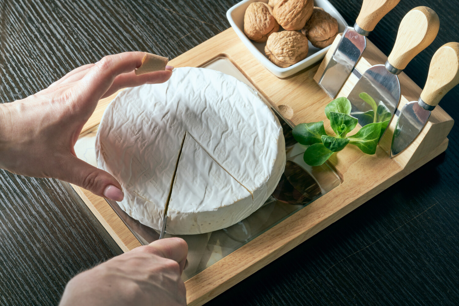 Hands slice brie on cutting board