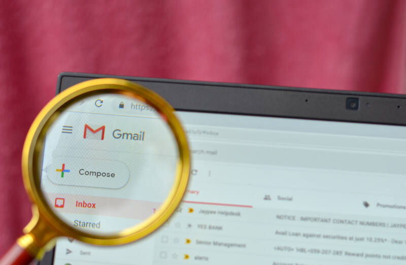 Gmail application open on a browser and logo seen through a magnifying lens. Out of focus laptop screen is in the background.