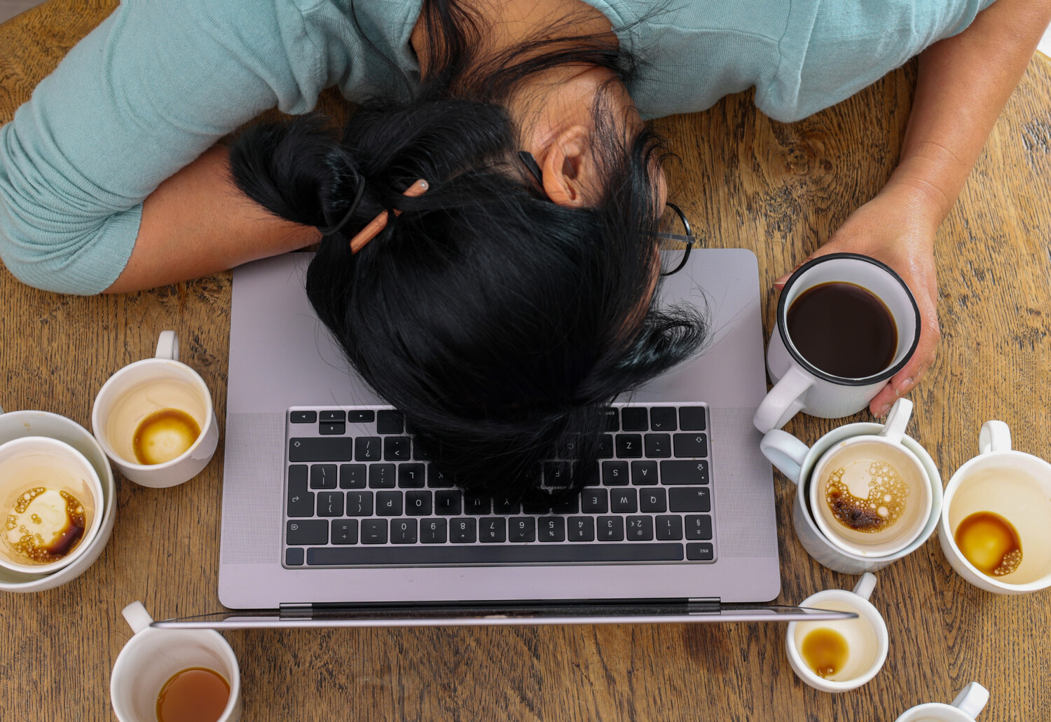 Exhausted worker with head on laptop surrounded by coffee cups