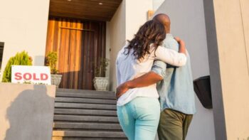 Couple embraces looking at home with sold sign