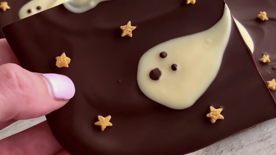 hand holding piece of chocolate with white chocolate ghost painted onto it