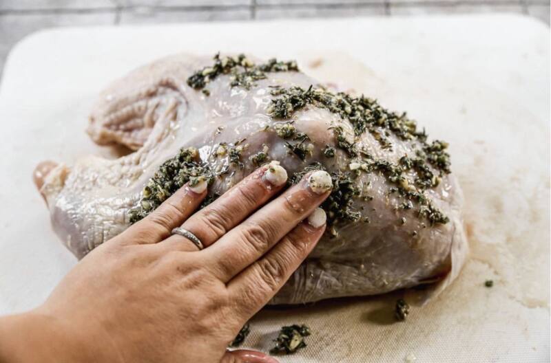 hand patting herbs and spices into raw turkey