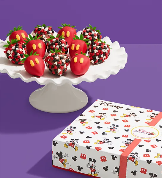 wrapped gift next to a white plate of chocolate covered berries decorated with mickey mouse sprinkles