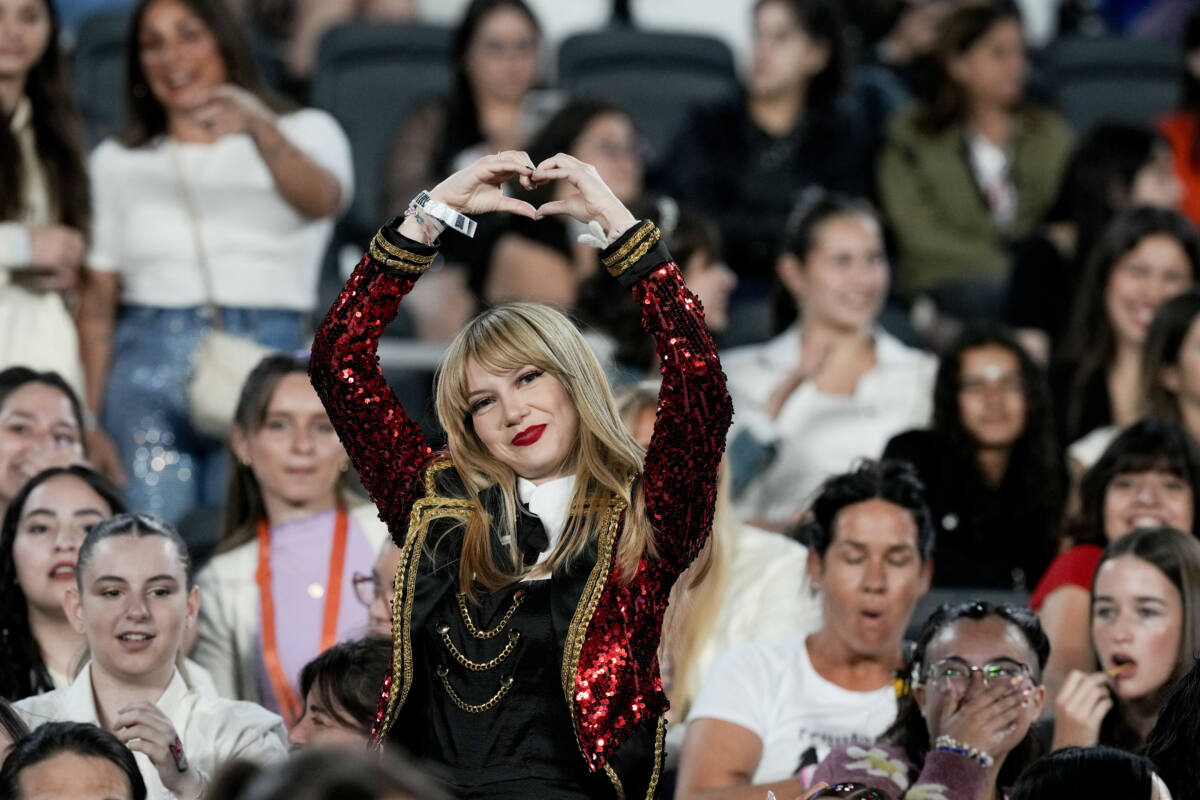 A Taylor Swift fan holds hands in heart above her head at concert