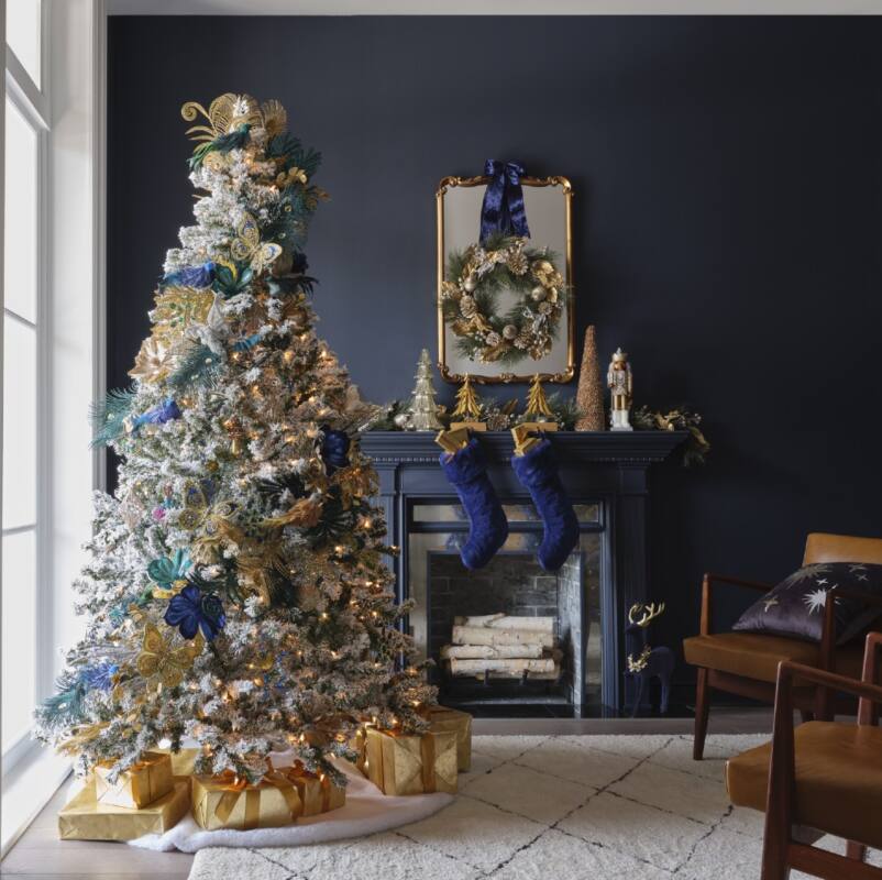 A room is decorated in shades of gold and deep navy with a Christmas tree and festive mantle.