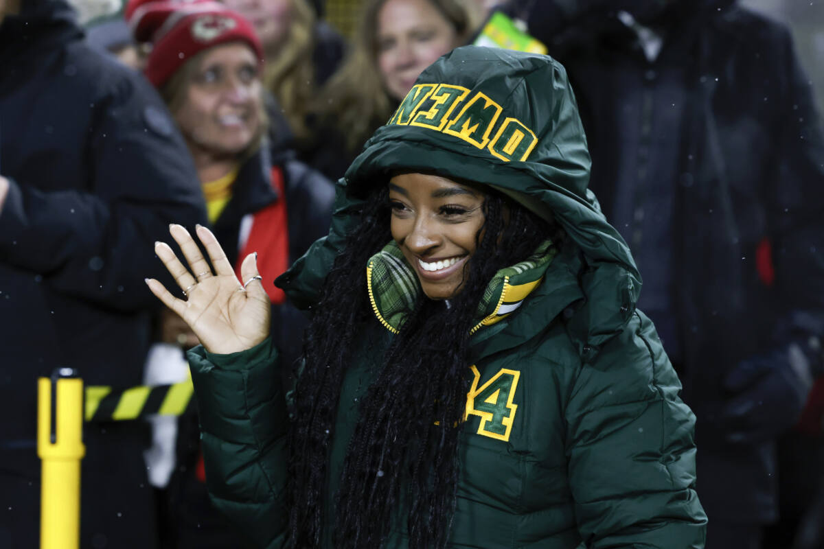 Simone Biles waves while watching her husband warm up at Packers game