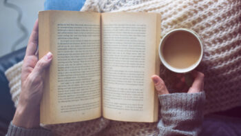 a woman is reading a book and holding coffee