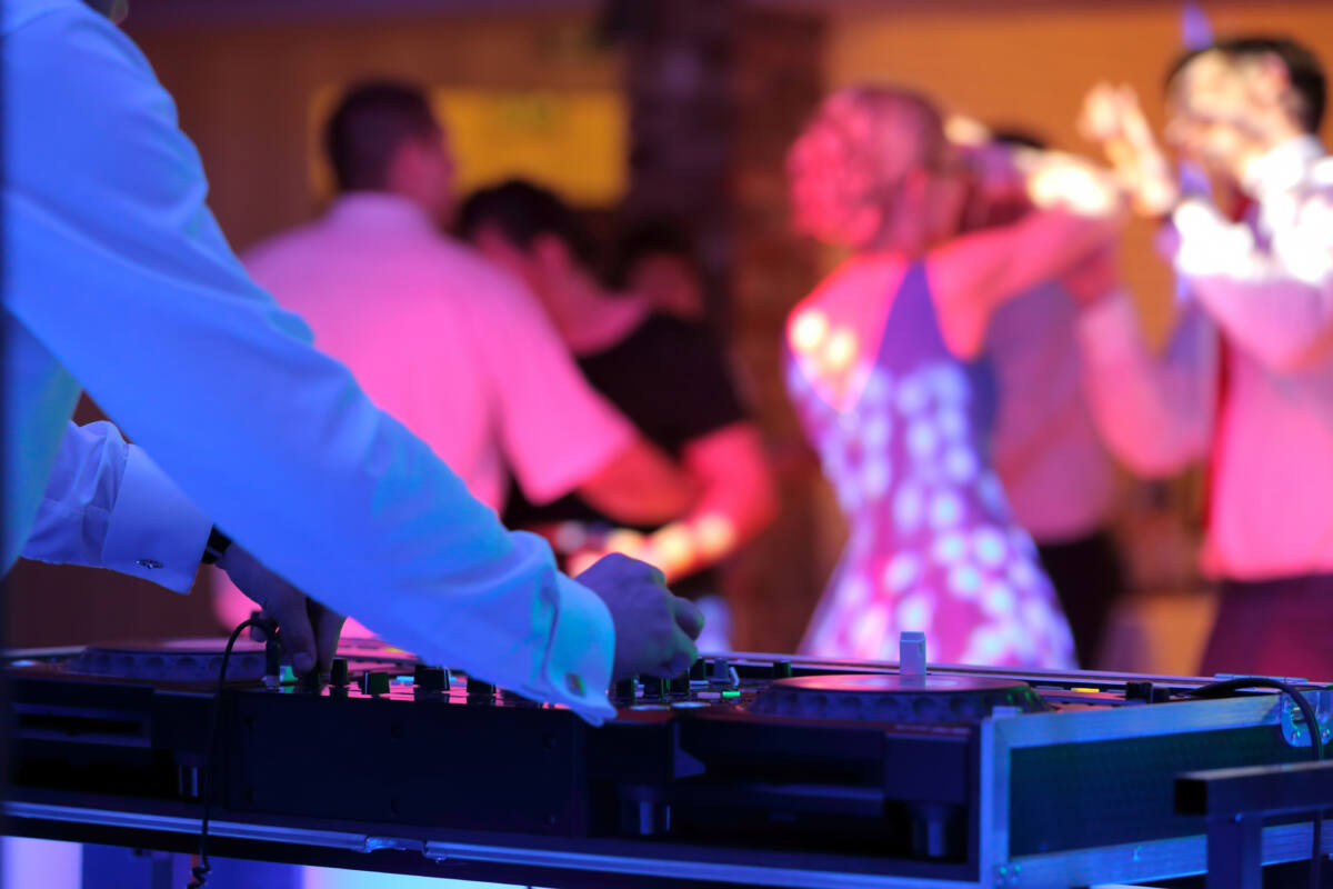 A DJ adjusts music levels while people dance in background.