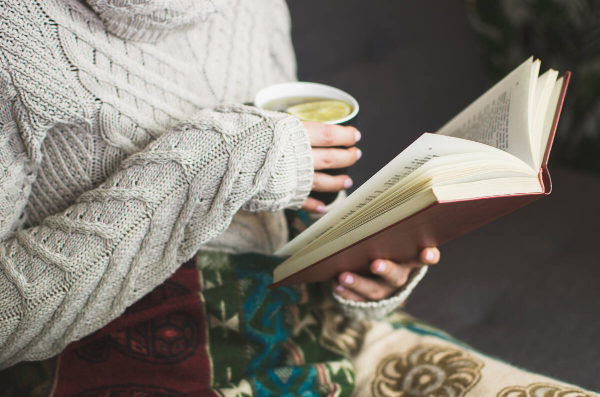 Woman reading a book while holding hot drink in a cozy place