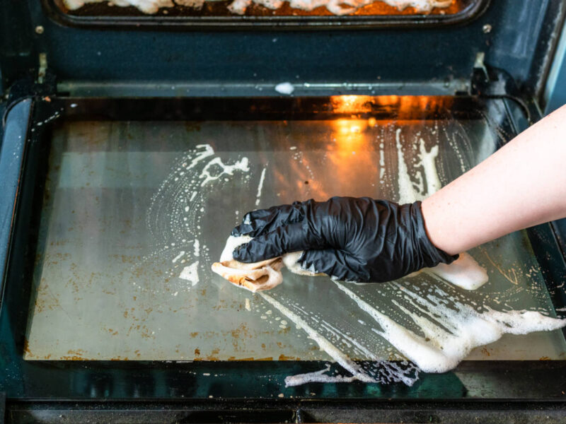 Photo of person cleaning a dirty glass oven door