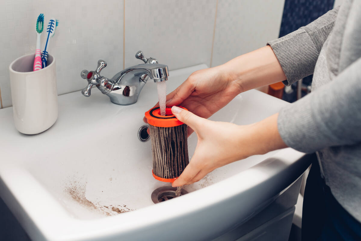 Woman washing filter with water in bathroom sink at home. 