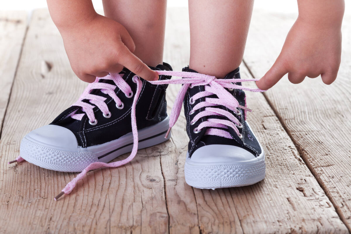 Little kid showing off tied, pink shoelaces on black high-top sneakers