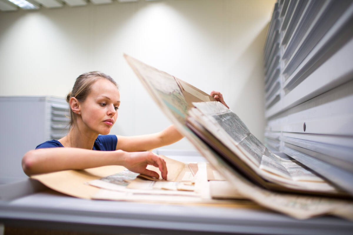 woman searching through maps in well-lit archive