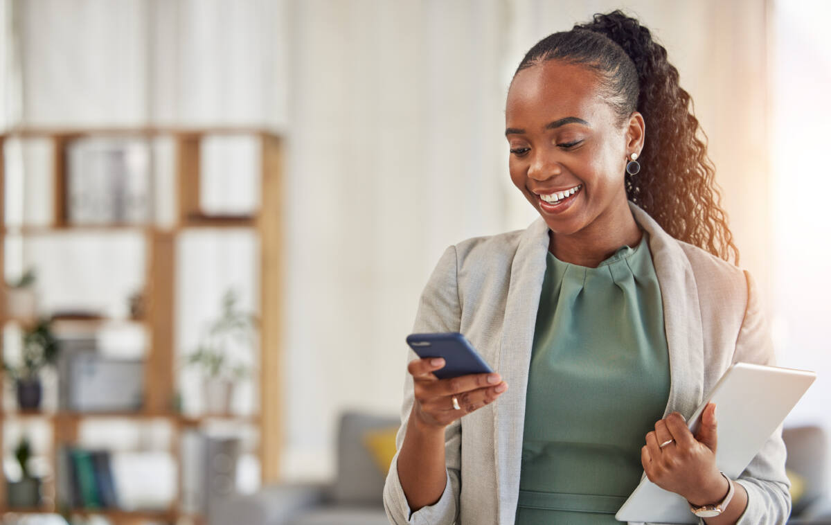 Happy black woman, phone and communication at office with smile in networking or social media. African female person or employee enjoying online browsing or chat on mobile smartphone app at workplace.