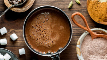 A look into a small pot of freshly made hot cocoa with ingredients to make it all around.