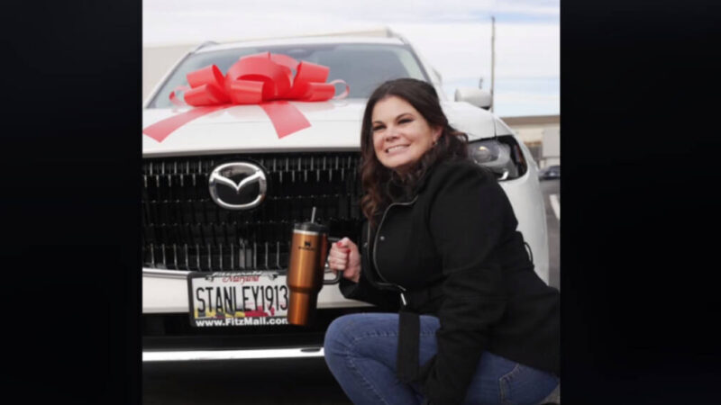 A TikToker poses with her new Stanley Quencher and the new white Mazda SUV that Stanley bought her