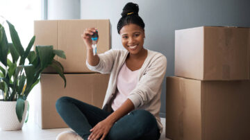Happy woman surrounded by moving boxes holds key to her new home