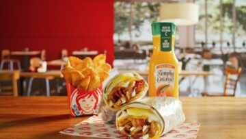 Wendy's new breakfast burrito alongside seasoned potatoes and a bottle of orange juice