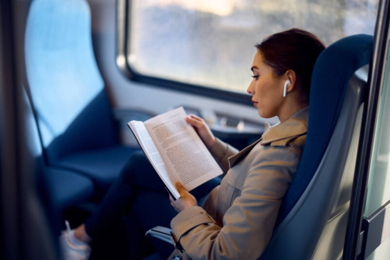Woman reads book while listening to music on train
