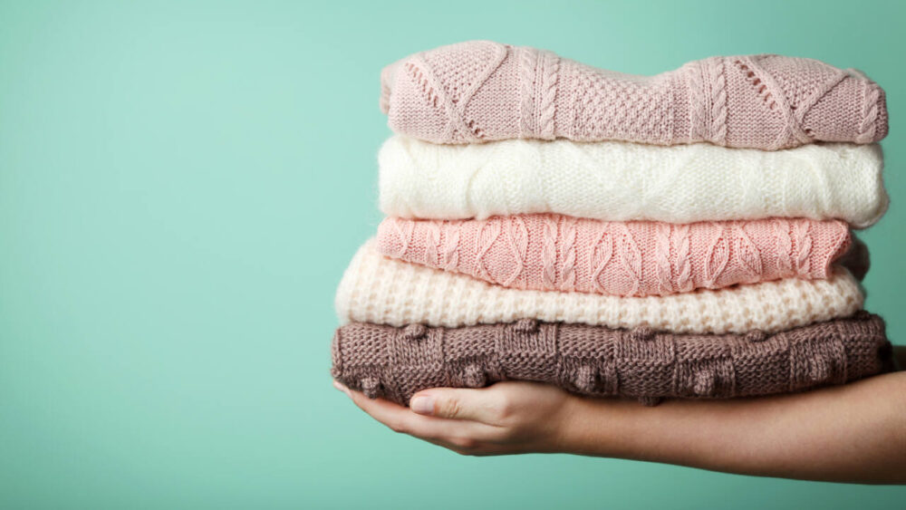 A person holds a stack of folded cashmere sweaters.