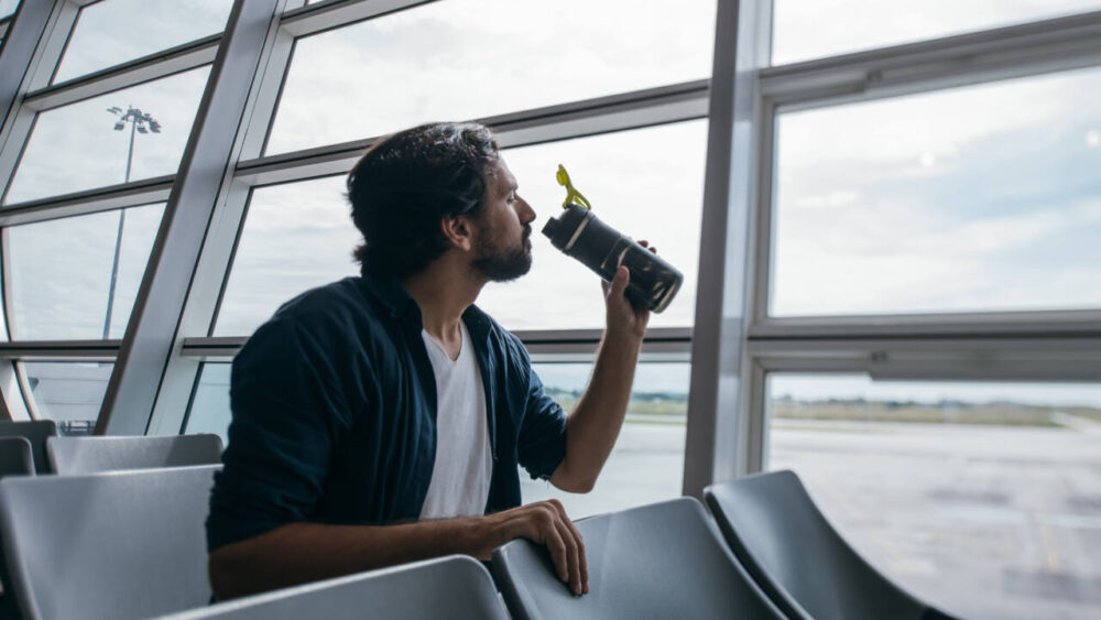 A man drinks from a water bottle in an airport.