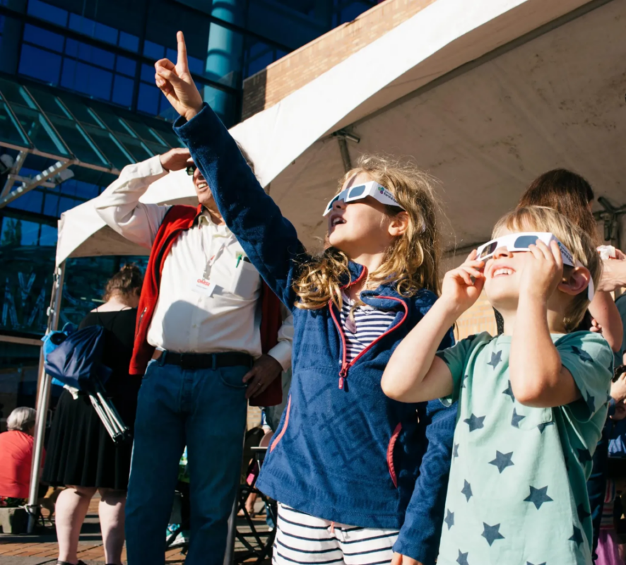 Two kids look at a solar eclipse through solar eclipse glasses