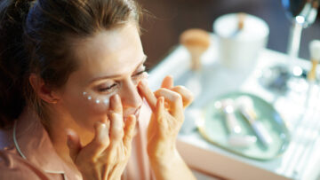 A woman applies eye cream over her vanity.
