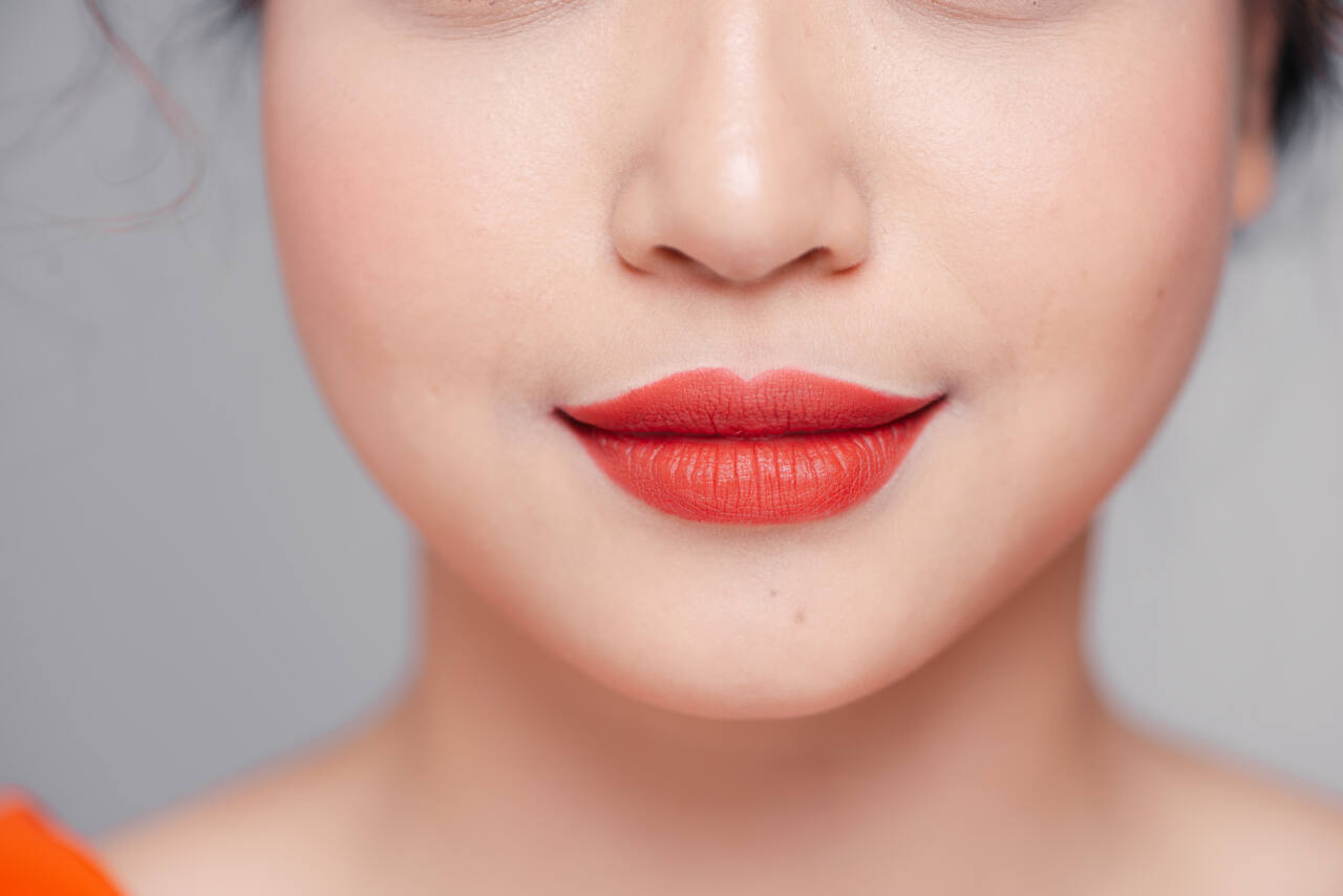 A woman wears a coral lipstick.