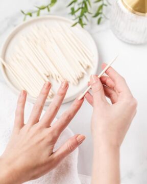 Image of woman using an orange wood stick for nails to push back cuticles.
