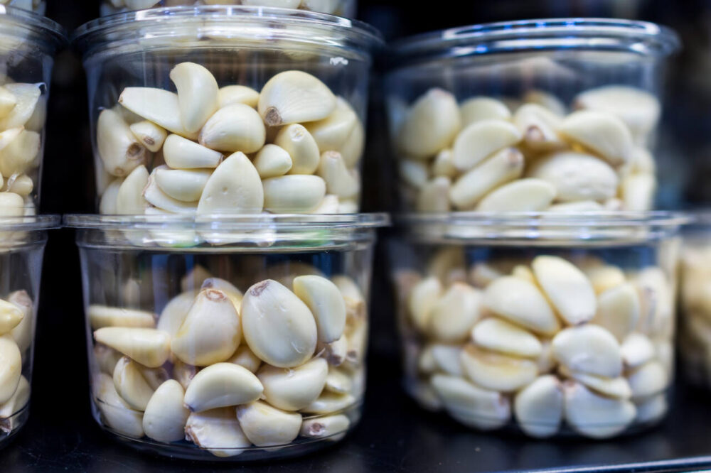 clear containers of peeled garlic cloves are seen at a grocery store
