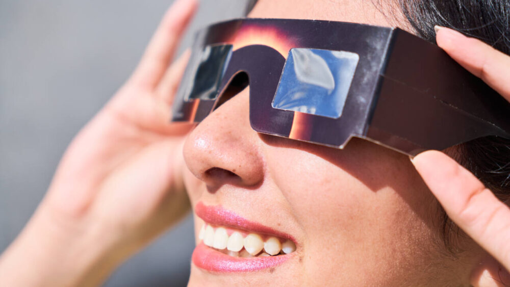 A woman views a solar eclipse while wearing glasses.